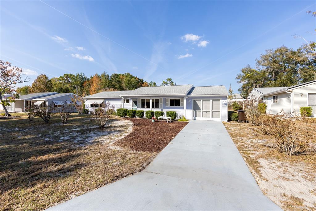 A light blue single-story house features a concrete driveway and a small front garden bed — 8987 SW 108TH PLACE, OCALA, FL