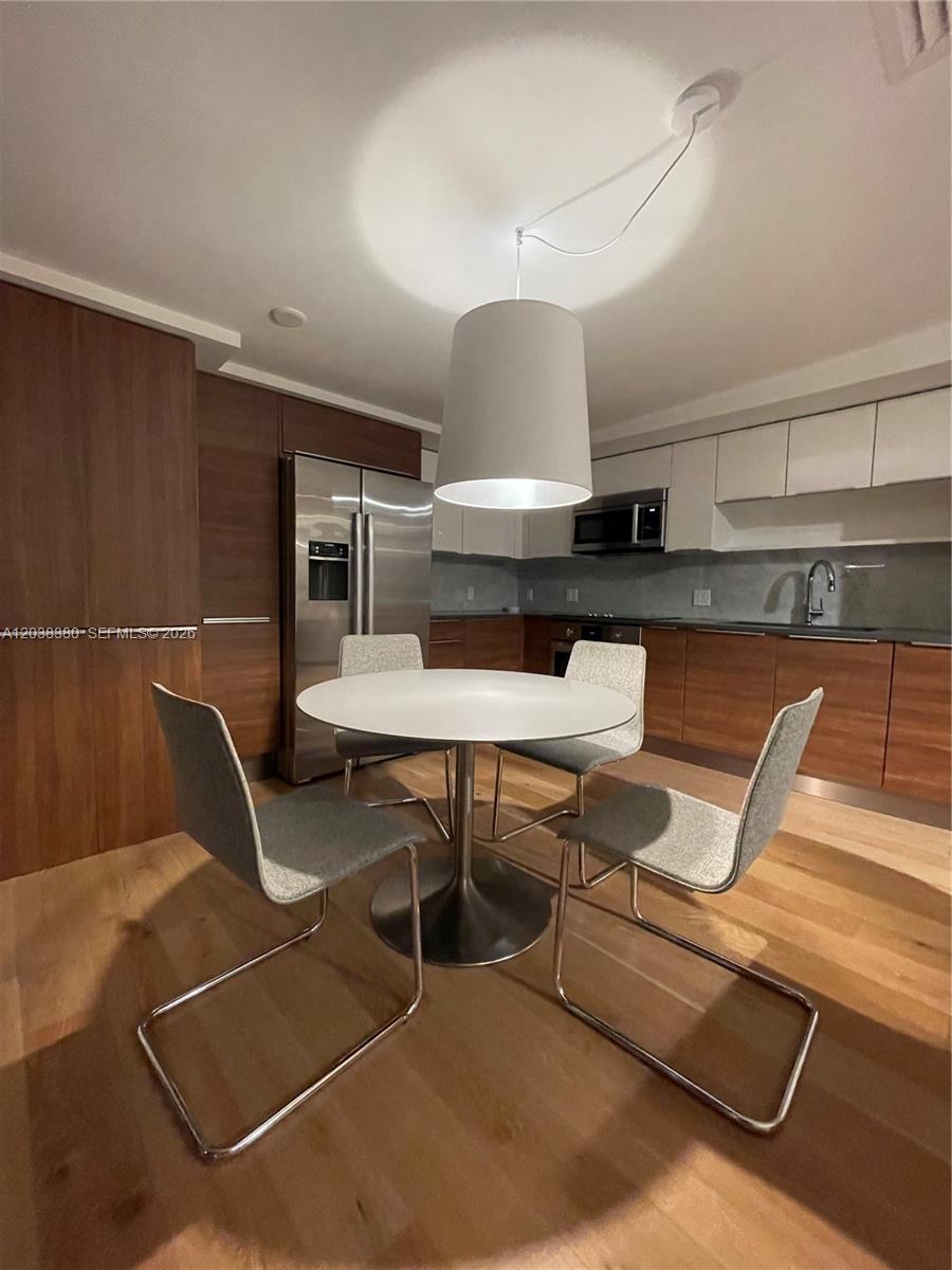 A modern kitchen features wood-toned lower cabinets, white upper cabinets, and a central dining area — 601 NE 27th St # 201, Miami FL 33137, MIAMI, FL