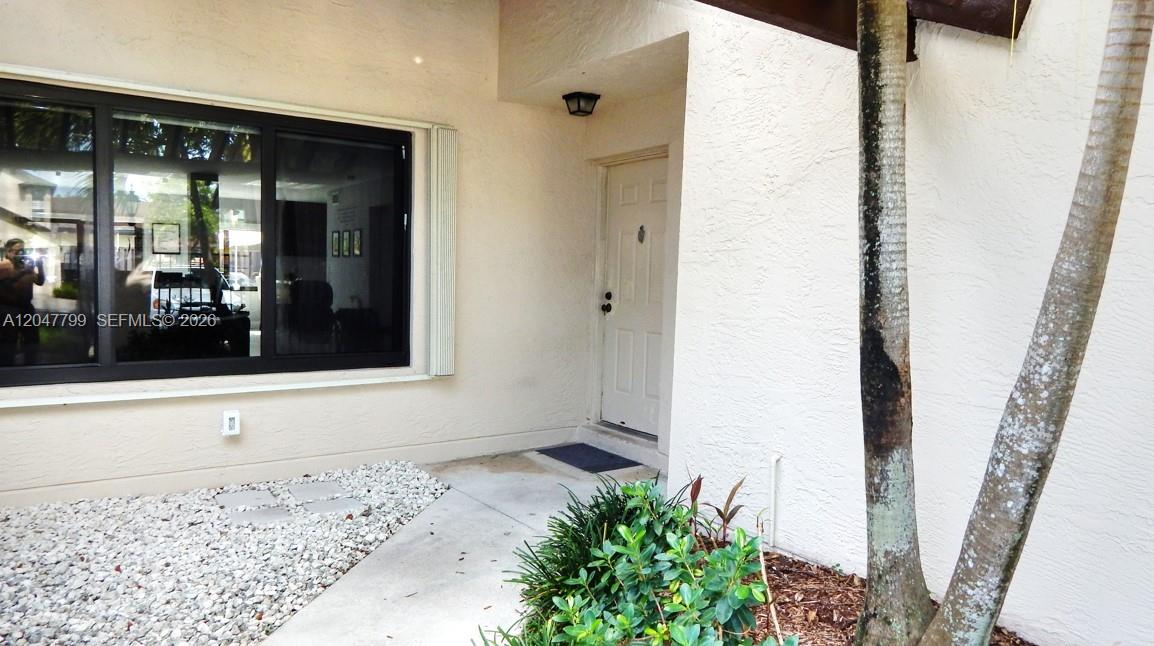 A white front door is recessed next to a large window and a palm tree — 10171 SW 137th Ct, Miami FL 33186, MIAMI, FL