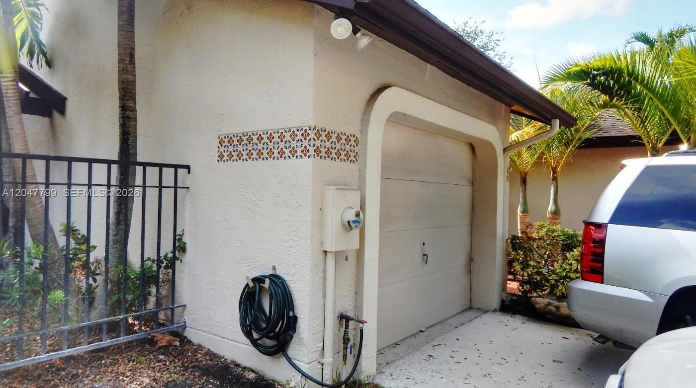 A white stucco garage exterior features a decorative tile accent and a black hose — 10171 SW 137th Ct, Miami FL 33186, MIAMI, FL