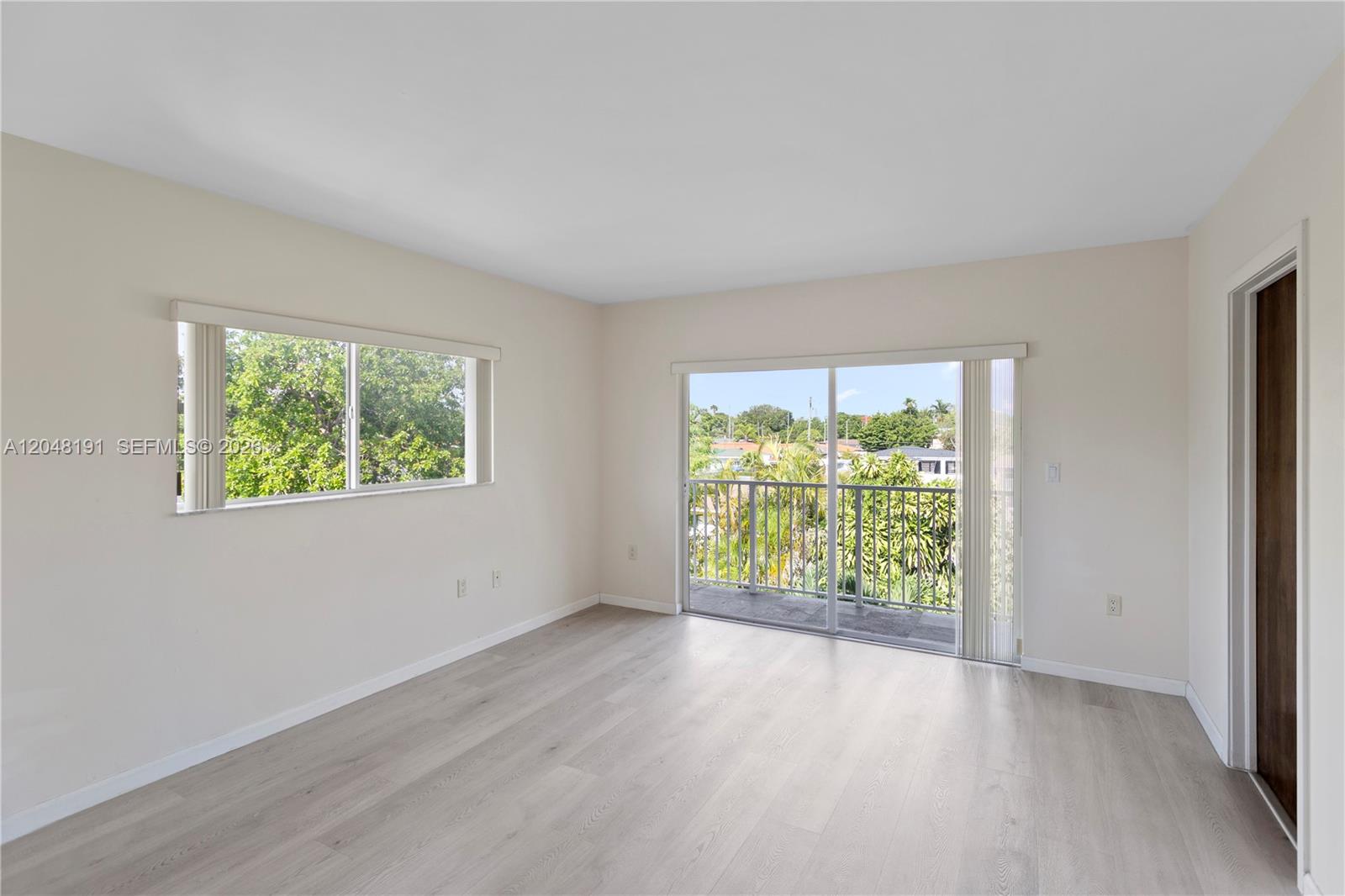 An empty bedroom features light wood-look flooring, a sliding glass door to a balcony, and windows — 2782 SW 33rd Ave # 2782, Miami FL 33133, MIAMI, FL