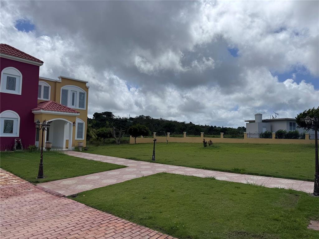 A two-story house with a red roof and yellow walls stands beside a grassy lawn — Camino Los Nieves LOS NIEVES 447 INT, ISABELA, PR