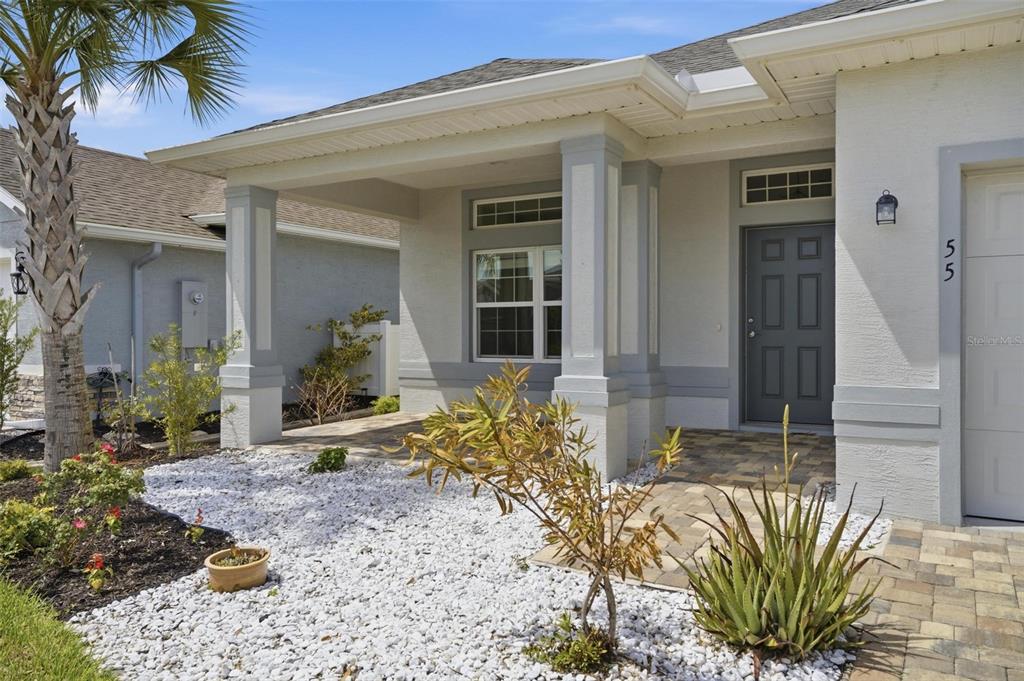 The exterior of a house features a covered porch, a grey front door, and landscaping — 55 MATANZAS LAKES DRIVE, PALM COAST, FL