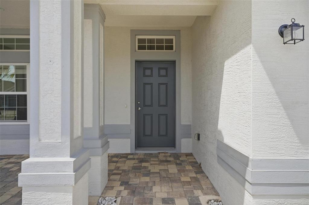 A covered entryway features a gray front door, a transom window, and paver flooring — 55 MATANZAS LAKES DRIVE, PALM COAST, FL