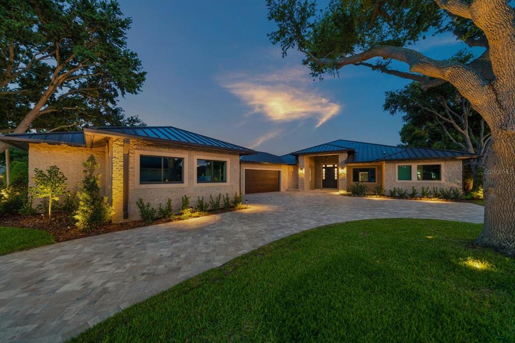 A modern single-story house with a stone facade, dark metal roof, and paved circular driveway — 19 HIBISCUS ROAD, BELLEAIR, FL