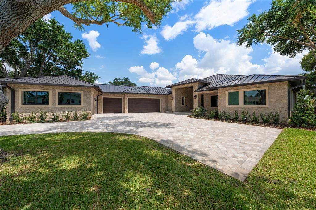 A single-story house with a stone facade, metal roof, and a large paved driveway — 19 HIBISCUS ROAD, BELLEAIR, FL