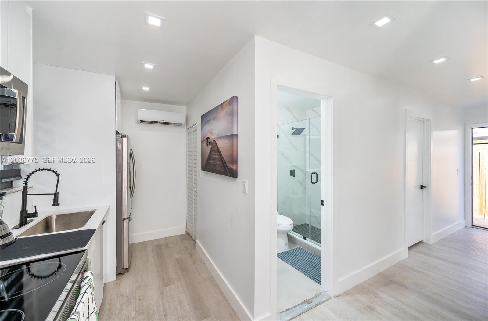 A modern kitchen area features white cabinetry, stainless steel appliances, and an adjacent bathroom entrance — 3016 NW 22nd Ct # 3018, Miami FL 33142, MIAMI, FL