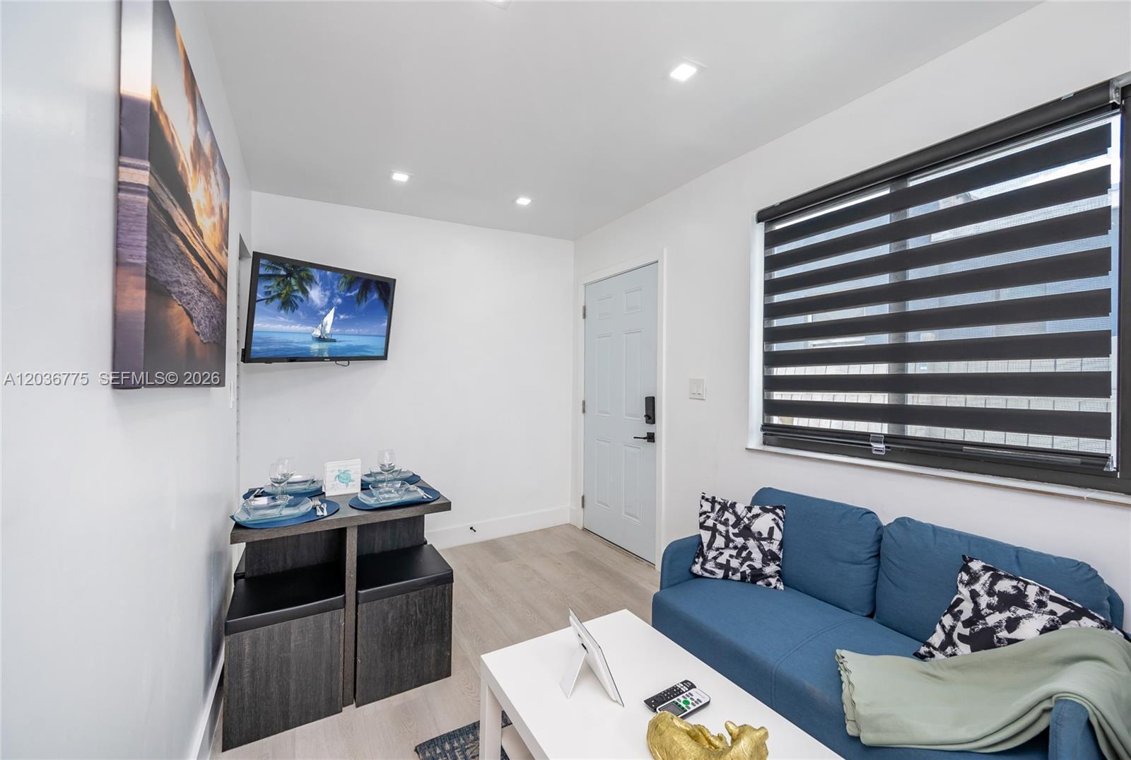 A small living room features a blue sofa, a dining set, and a wall-mounted television — 3016 NW 22nd Ct # 3018, Miami FL 33142, MIAMI, FL