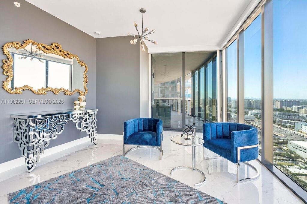 A modern room features two blue velvet chairs, a mirrored console table, and floor-to-ceiling windows — SUNNY ISLES BEACH, FL