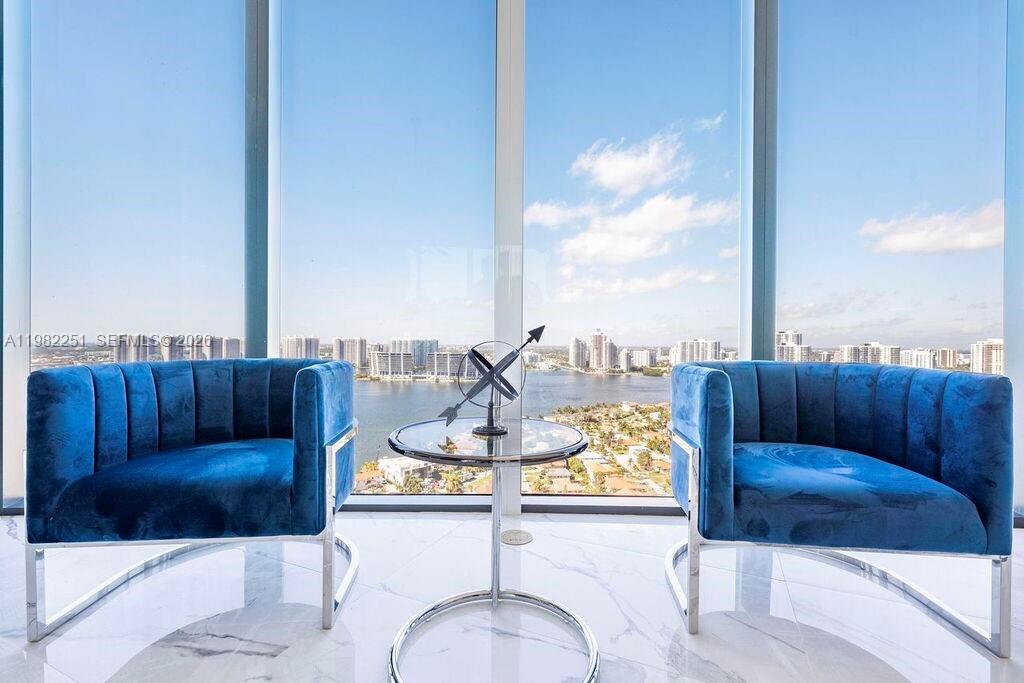 Two blue velvet armchairs face a glass table in front of floor-to-ceiling windows — SUNNY ISLES BEACH, FL