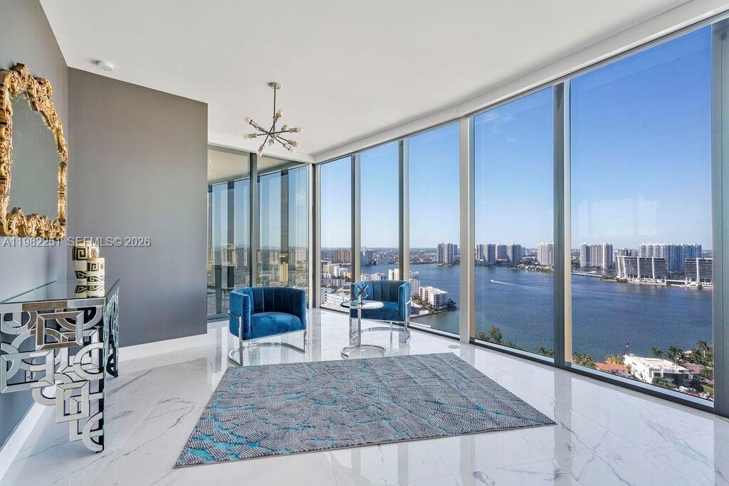A modern living area features floor-to-ceiling windows with a waterfront view and marble flooring — SUNNY ISLES BEACH, FL