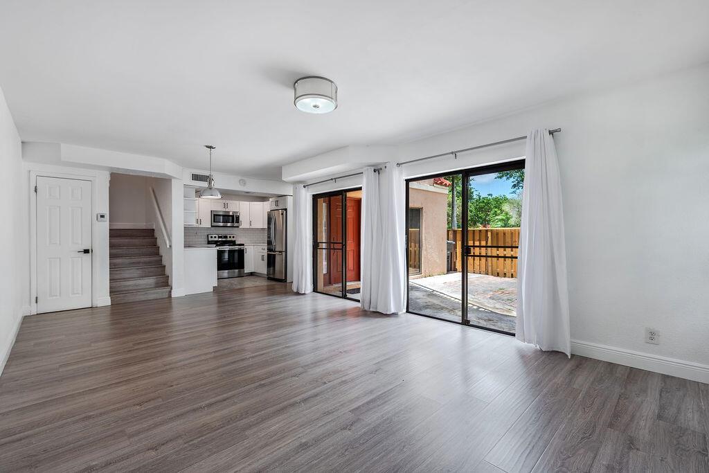 An open-concept living area with wood-look flooring, a kitchen, and sliding glass doors to a patio — 8050 Severn Drive # C, Boca Raton FL 33433, BOCA RATON, FL