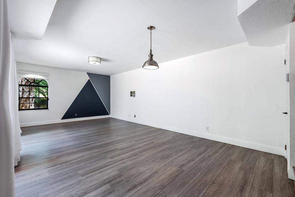 An empty room with wood-look flooring, white walls, a geometric accent wall, and pendant lighting — 8050 Severn Drive # C, Boca Raton FL 33433, BOCA RATON, FL