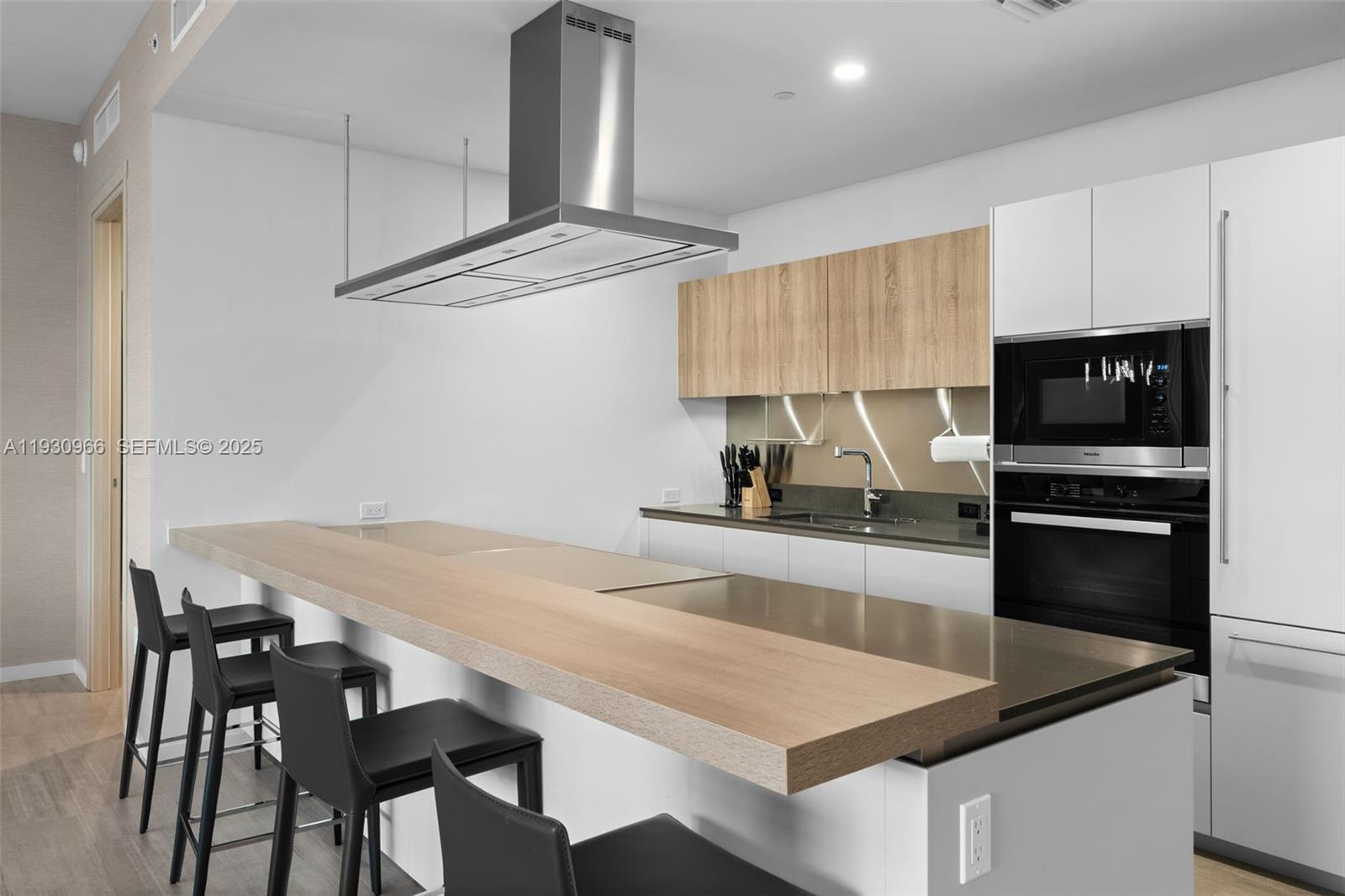 A modern kitchen features a wooden breakfast bar, stainless steel range hood, and white cabinetry — 1000 Brickell Plz, Miami FL 33131, MIAMI, FL