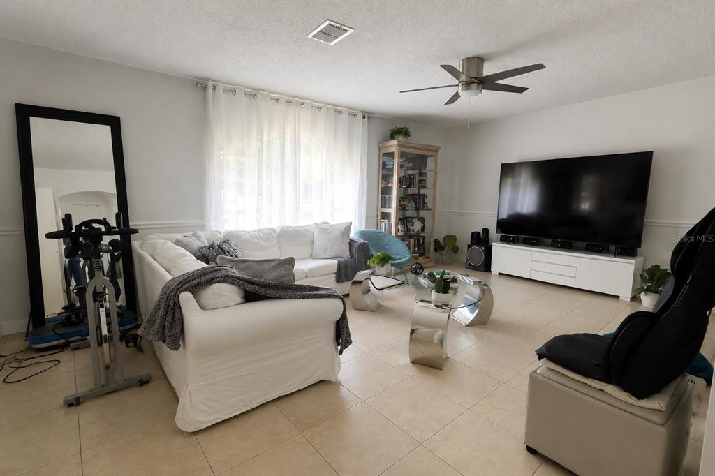 A living room features a white sectional sofa, a large television, and a glass coffee table — 984 DERBYSHIRE DRIVE, KISSIMMEE, FL