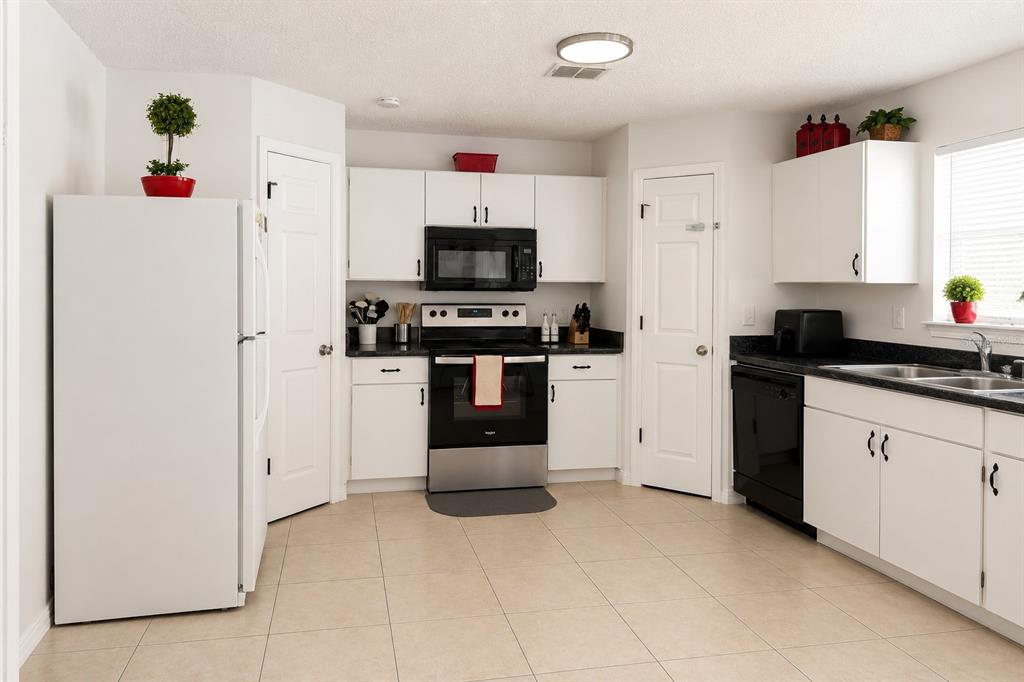 A kitchen features white cabinets, black appliances, dark countertops, and light tile flooring — 984 DERBYSHIRE DRIVE, KISSIMMEE, FL