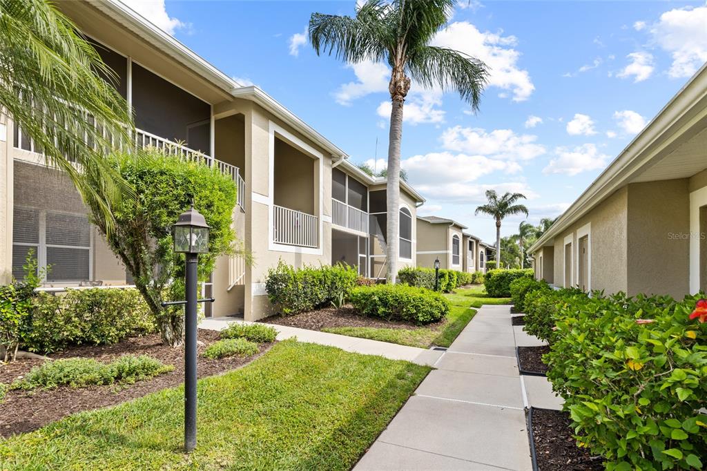 A sidewalk leads between two tan apartment buildings with screened balconies and palm trees — 5231 MAHOGANY RUN AVENUE UNIT 325, SARASOTA, FL
