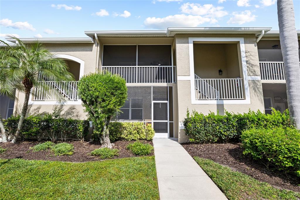 A two-story apartment building exterior features a screened-in entryway, white railings, and landscaped bushes — 5231 MAHOGANY RUN AVENUE UNIT 325, SARASOTA, FL