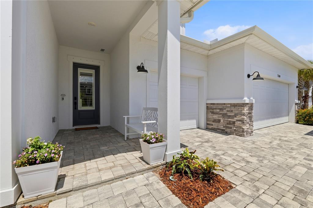A paved walkway leads to a covered front porch with a dark door and garage — 7530 ASHBROOKE PINE LOOP, ODESSA, FL