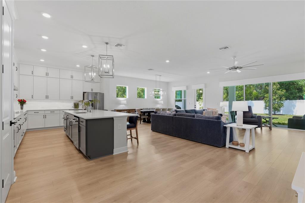 An open-concept kitchen and living area with white cabinetry, a dark island, and hardwood floors — 7530 ASHBROOKE PINE LOOP, ODESSA, FL