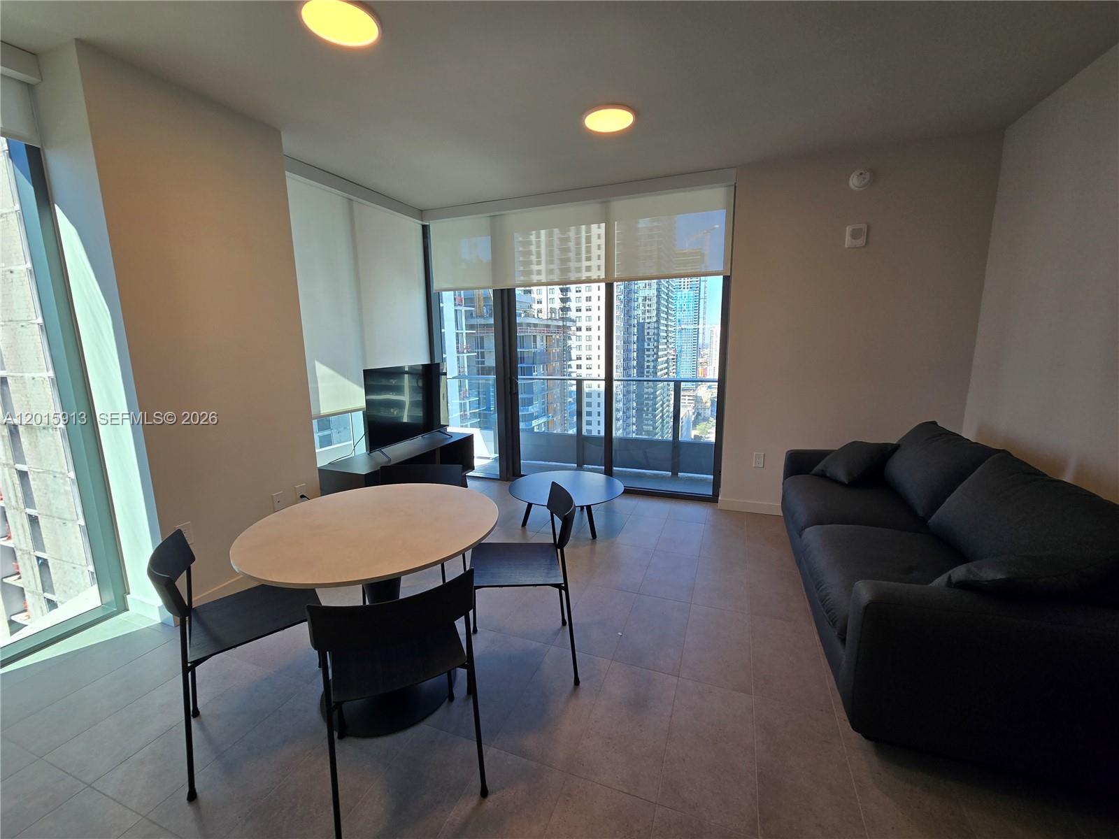 A modern living and dining area features tile floors, a dark sofa, and floor-to-ceiling windows — 121 NE 5 ST # 2908, Miami FL 33132, MIAMI, FL
