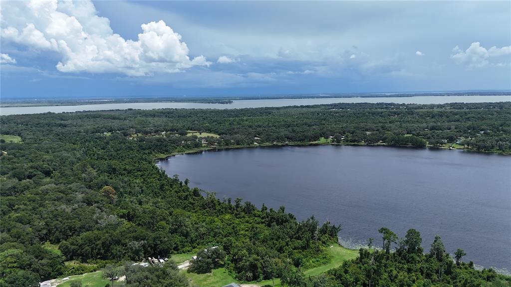 An aerial view shows a large lake surrounded by dense forest under a cloudy sky — CLARK ROAD, FRUITLAND PARK, FL