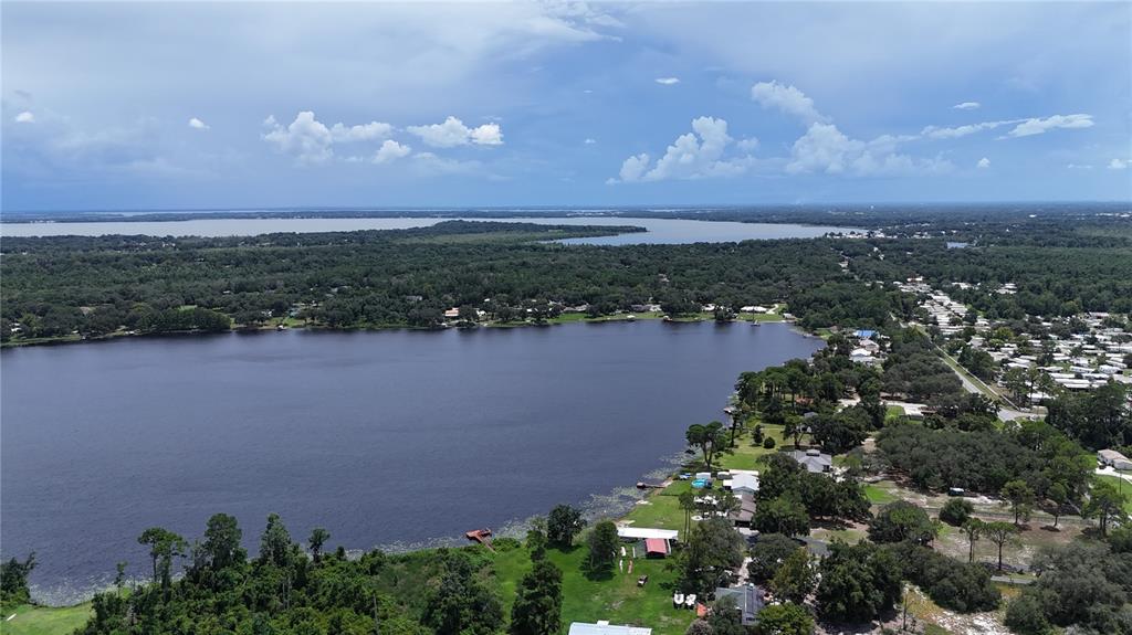 An aerial view shows a large lake surrounded by trees and residential properties under a cloudy sky — CLARK ROAD, FRUITLAND PARK, FL