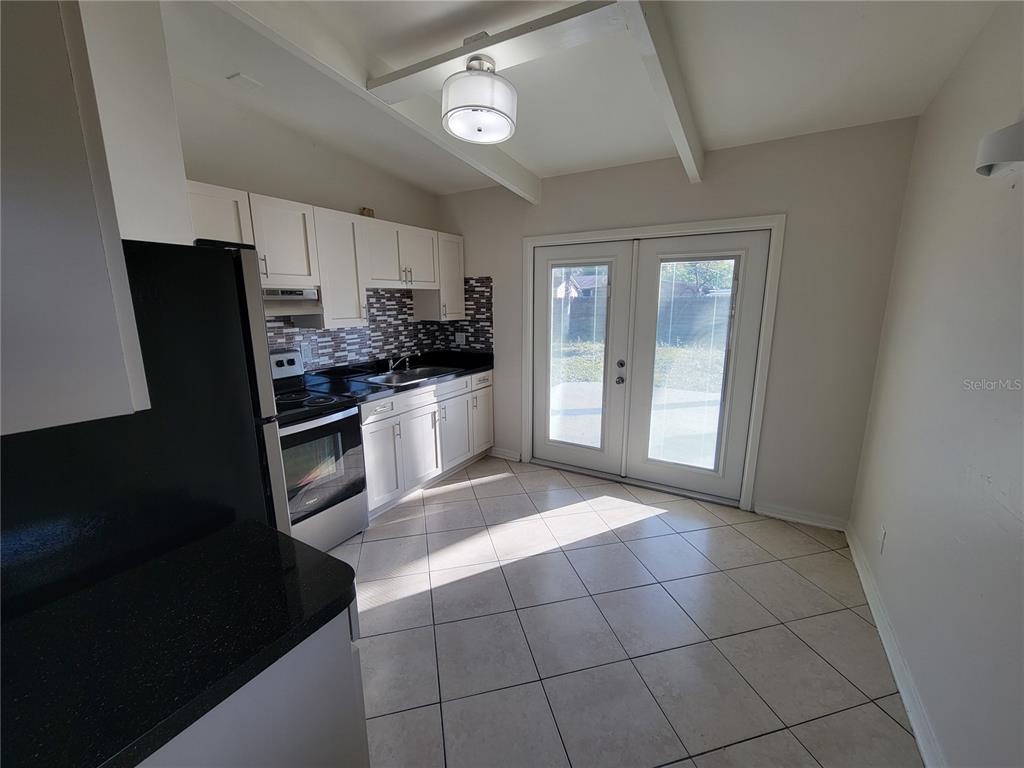 A kitchen features white cabinets, black countertops, a tile backsplash, and French doors — 1212 WINDERMERE WAY, TAMPA, FL