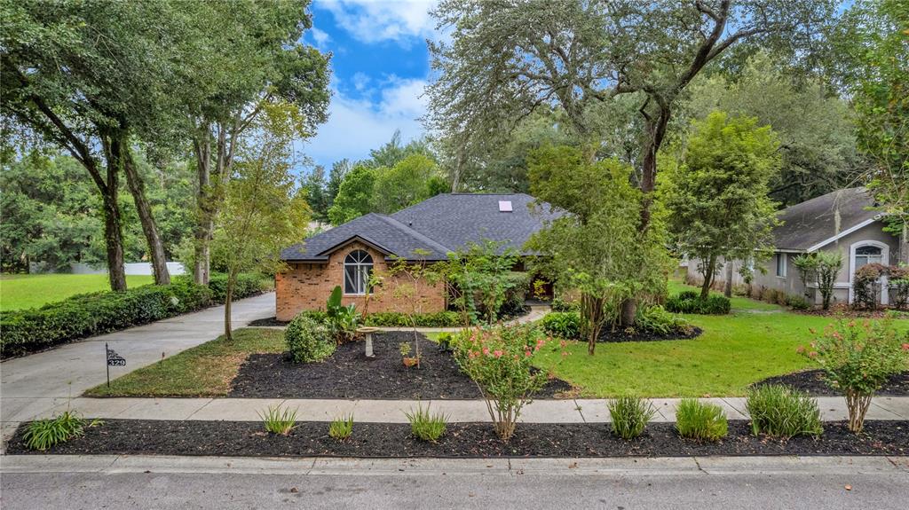 A one-story brick house with a dark shingled roof sits behind a landscaped front yard — 329 SUN OAKS COURT, LAKE MARY, FL