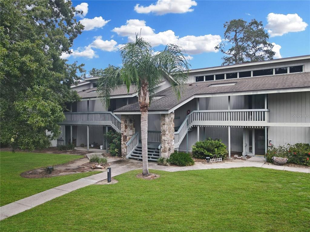 A two-story apartment building with gray siding, stone pillars, and exterior wooden staircases — 3566 CAMELOT DRIVE UNIT 6, HAINES CITY, FL