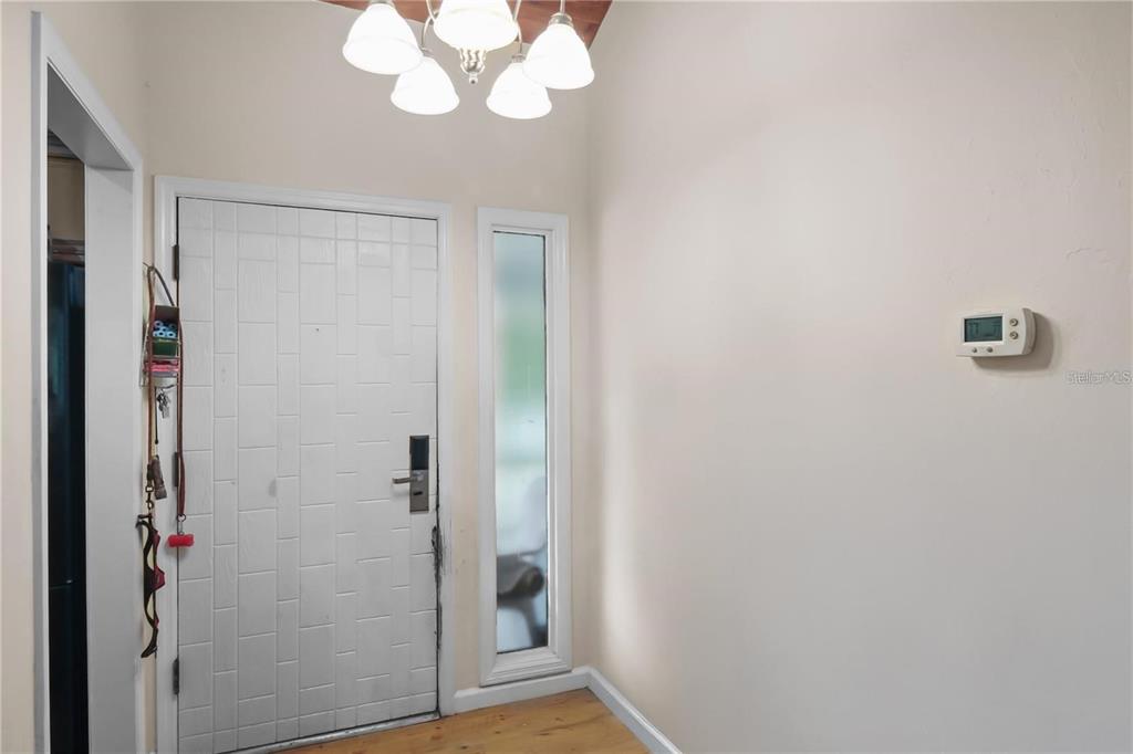 An entryway features a white door with a sidelight, a chandelier, and a wall thermostat — 3566 CAMELOT DRIVE UNIT 6, HAINES CITY, FL