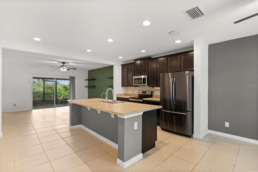 A kitchen features dark wood cabinets, stainless steel appliances, a granite island, and tile flooring — 322 ANNABELLE WAY, DAVENPORT, FL