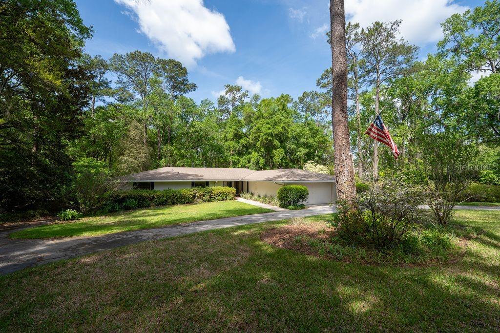 A single-story ranch-style house with a driveway sits among mature trees and green landscaping — 412 NW 46TH STREET, GAINESVILLE, FL