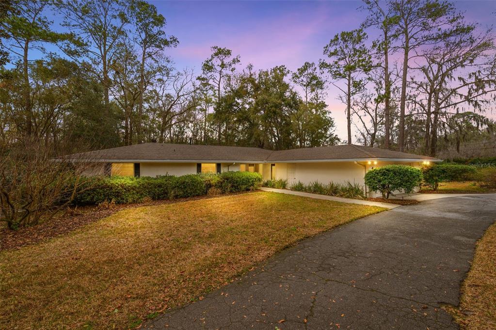 A single-story house with a white exterior and a driveway sits among tall trees — 412 NW 46TH STREET, GAINESVILLE, FL
