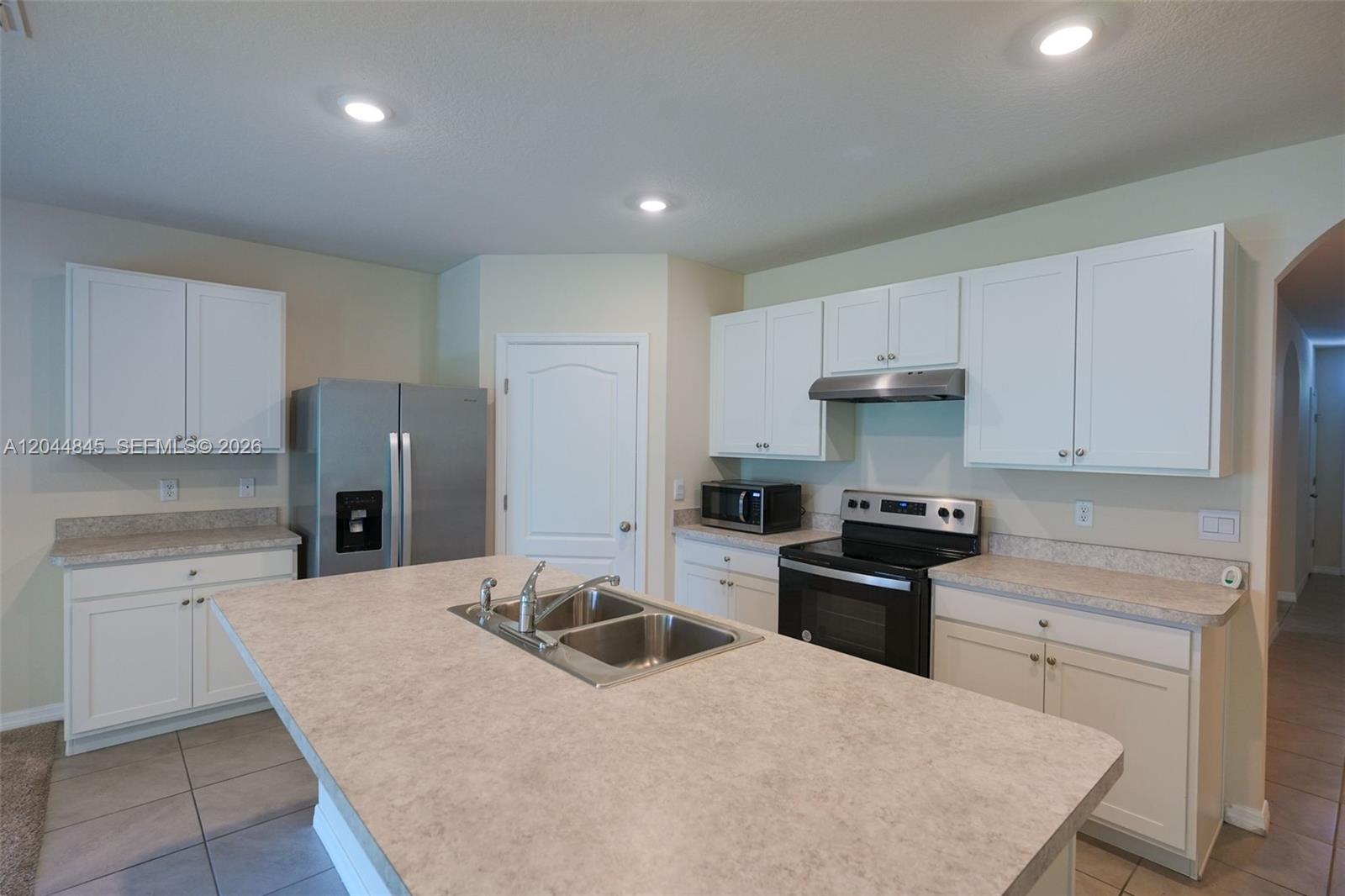 A kitchen features white cabinets, a central island with a sink, and stainless steel appliances — 660 COTULLA Dr, Kissimmee FL 34758, KISSIMMEE, FL
