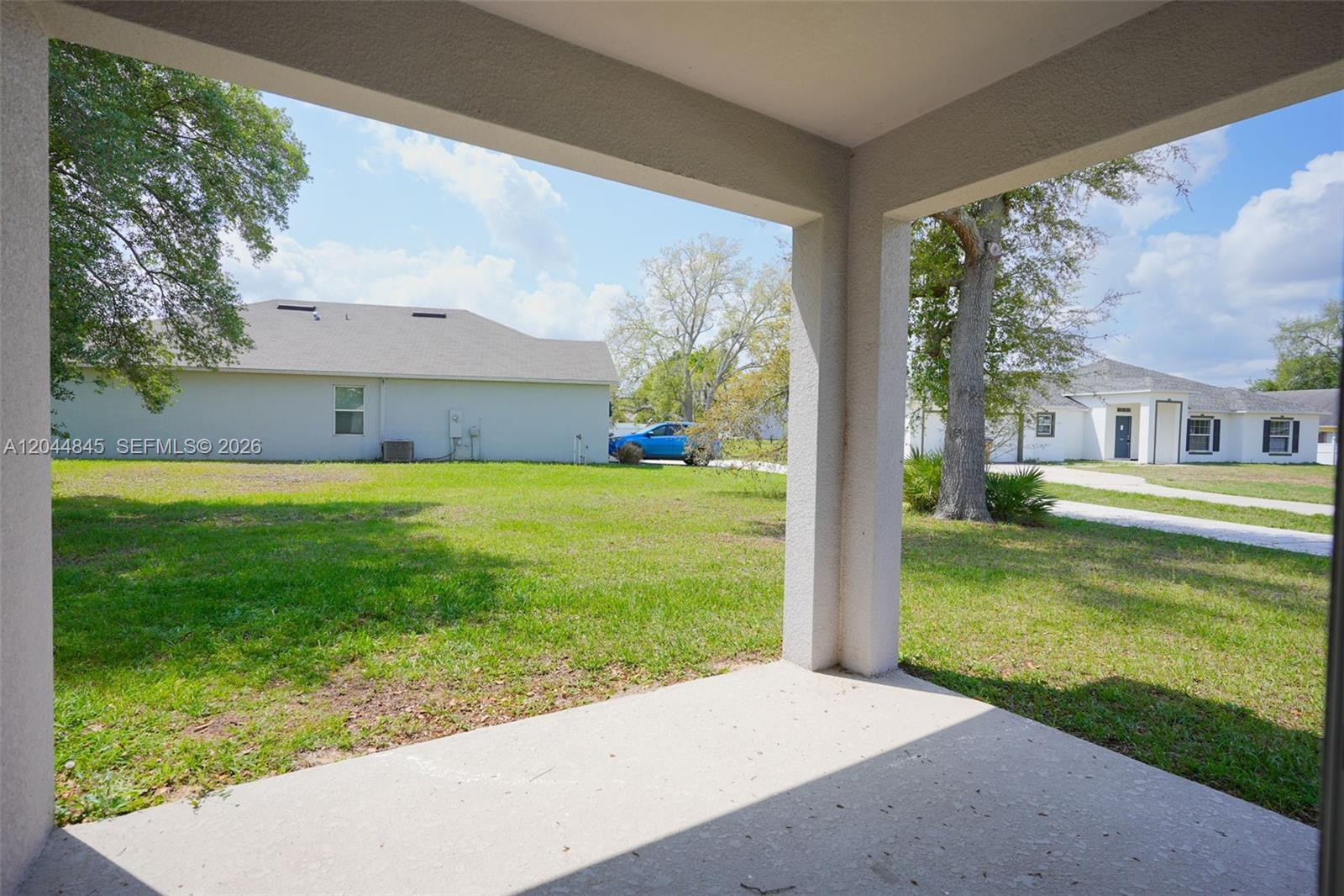 A concrete patio overlooks a grassy backyard with neighboring houses and a blue car — 660 COTULLA Dr, Kissimmee FL 34758, KISSIMMEE, FL