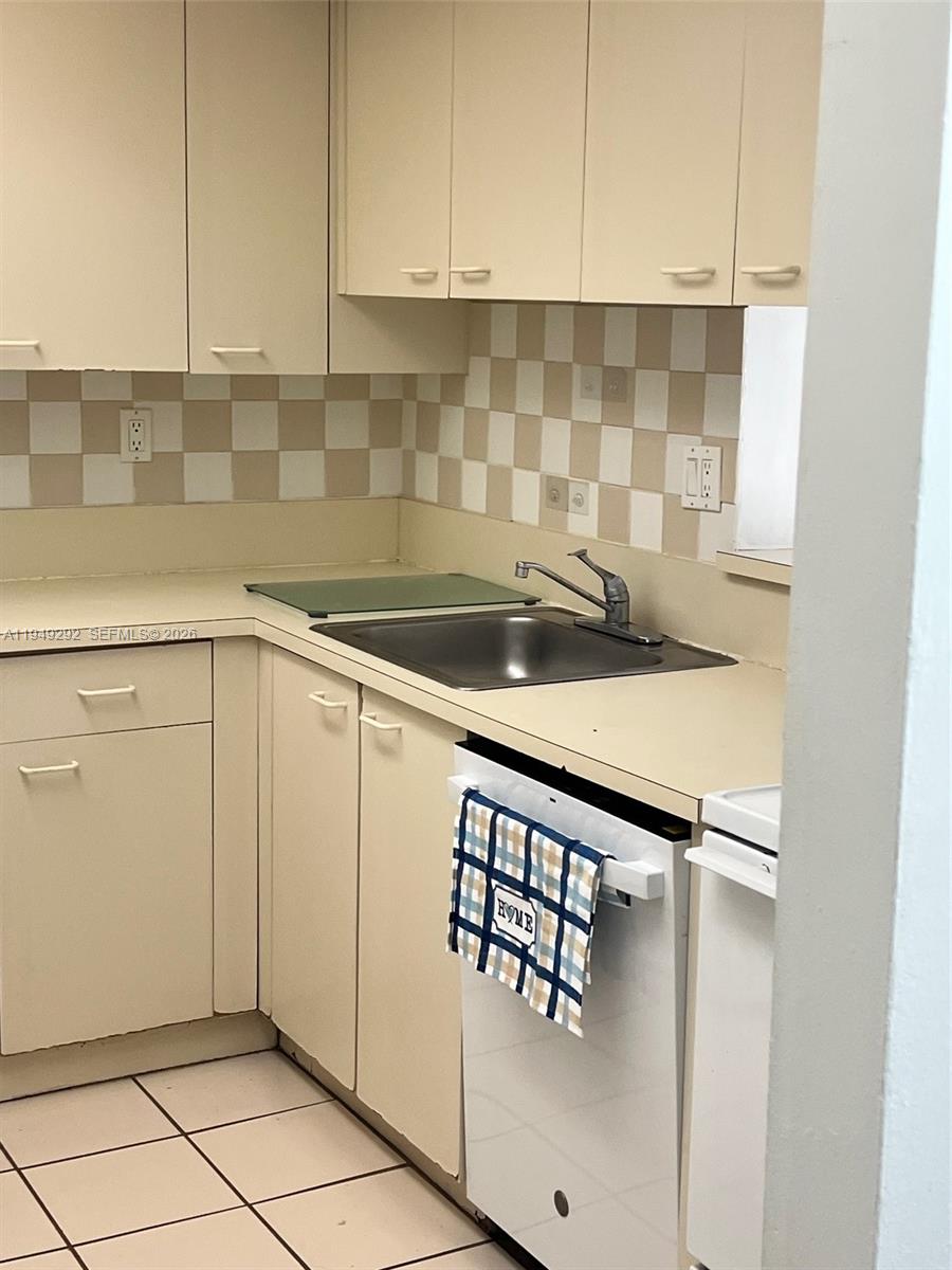 A small kitchen features beige cabinets, a checkered backsplash, and a white dishwasher — 10431 N Kendall Dr # D314, Miami FL 33176, MIAMI, FL