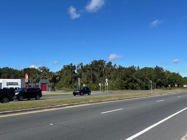 A paved road runs in front of a grassy lot with trees and nearby buildings — TBD US HWY 19 (N YOUNG BLVD), CHIEFLAND, FL