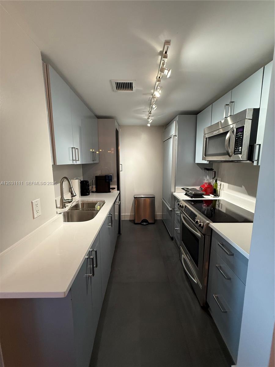 A galley kitchen features light blue cabinets, stainless steel appliances, and white countertops — 10275 Collins Ave # 921, Bal Harbour FL 33154, BAL HARBOUR, FL