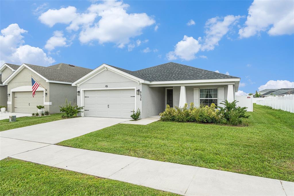 A single-story suburban house features a gray stucco exterior, a two-car garage, and landscaping — 6436 PEBBLEBROOKE WAY, ZEPHYRHILLS, FL