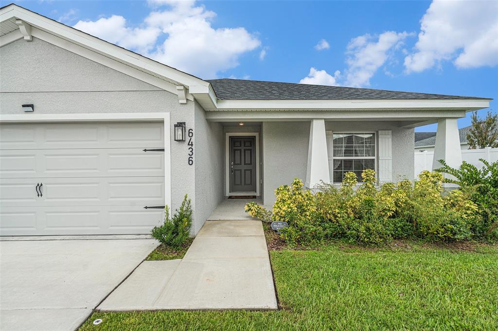 A single-story house exterior features a gray garage, a front entrance, and landscaped bushes — 6436 PEBBLEBROOKE WAY, ZEPHYRHILLS, FL