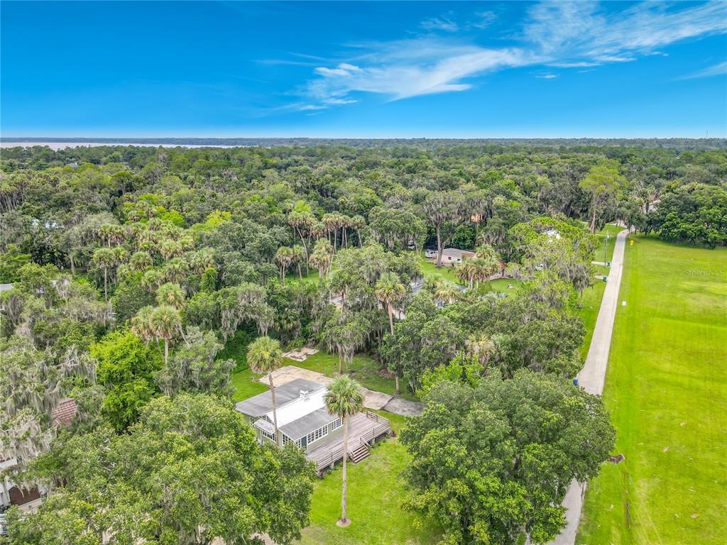 An aerial view shows a house with a deck surrounded by trees near a road — 556 STONE ISLAND ROAD, ENTERPRISE, FL