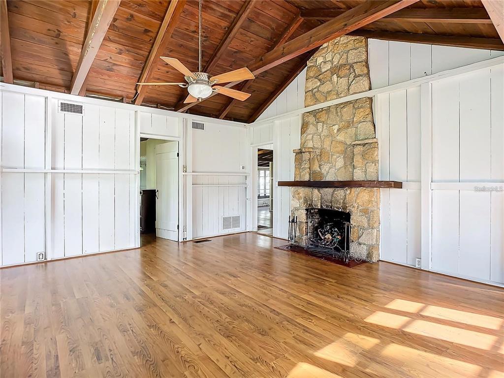A living room features a stone fireplace, vaulted wood-beam ceiling, and hardwood flooring — 556 STONE ISLAND ROAD, ENTERPRISE, FL