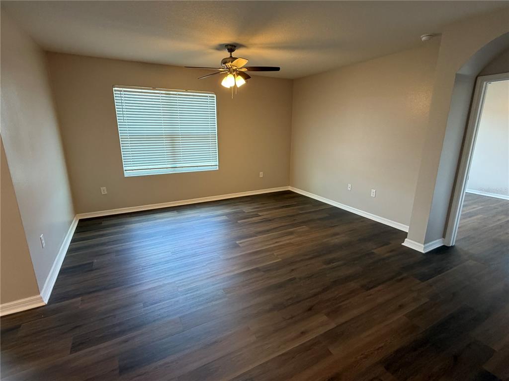An empty room features dark wood-look flooring, beige walls, a ceiling fan, and a window — 2822 NE 44TH ROAD, OCALA, FL