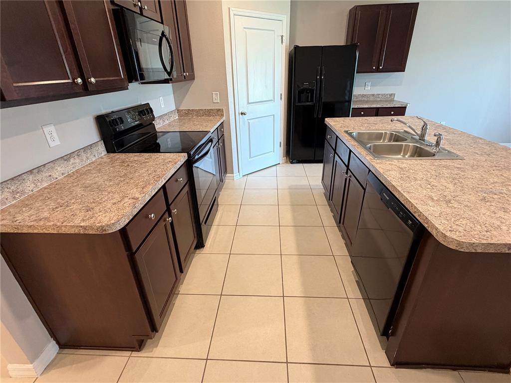A kitchen features dark wood cabinets, laminate countertops, black appliances, and light-colored floor tiles — 2822 NE 44TH ROAD, OCALA, FL
