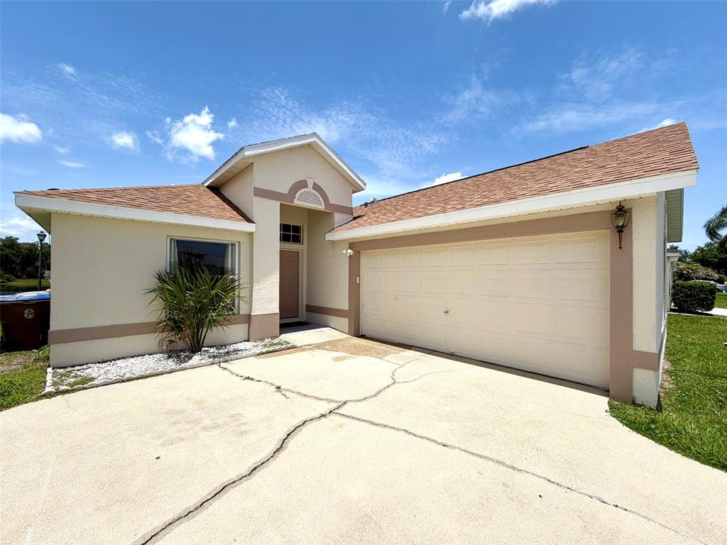 A single-story house with a beige stucco exterior, a two-car garage, and a cracked driveway — 2705 CHATHAM CIRCLE, KISSIMMEE, FL