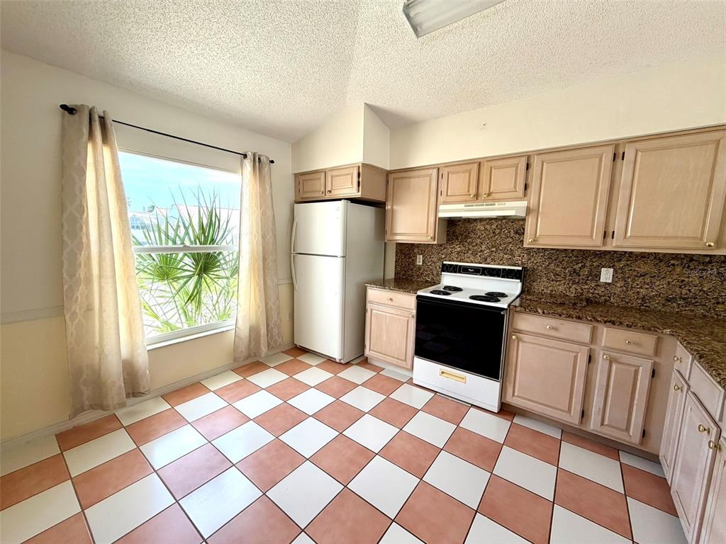 A kitchen features light wood cabinets, granite countertops, a white appliance suite, and checkered tile flooring — 2705 CHATHAM CIRCLE, KISSIMMEE, FL