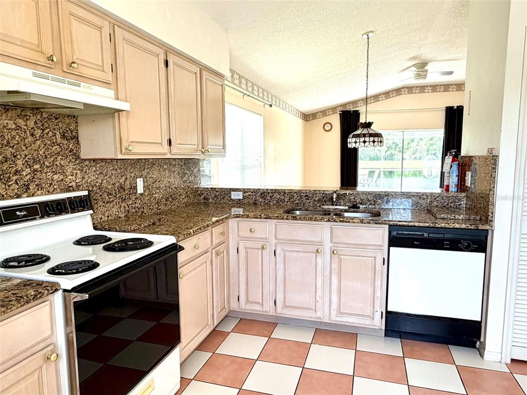 A kitchen features light wood cabinets, granite countertops, a white stove, and checkered tile flooring — 2705 CHATHAM CIRCLE, KISSIMMEE, FL