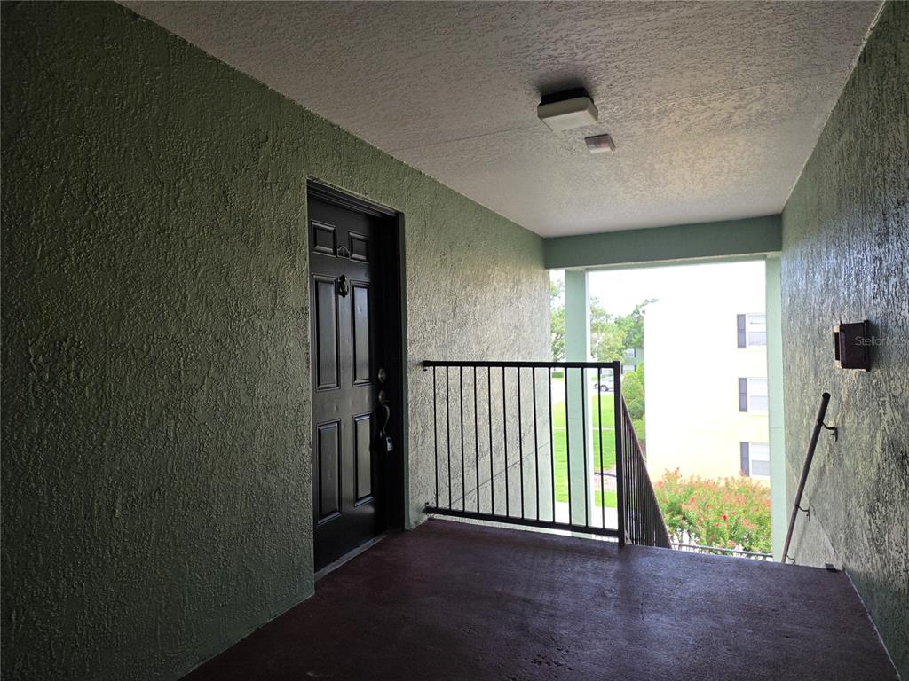 An exterior apartment entryway features a dark door, textured green walls, and a metal railing — 2031 DIXIE BELLE DRIVE UNIT 2031I, ORLANDO, FL