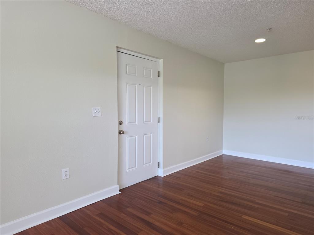 An empty room features white walls, dark wood-look flooring, and a white entry door — 2031 DIXIE BELLE DRIVE UNIT 2031I, ORLANDO, FL